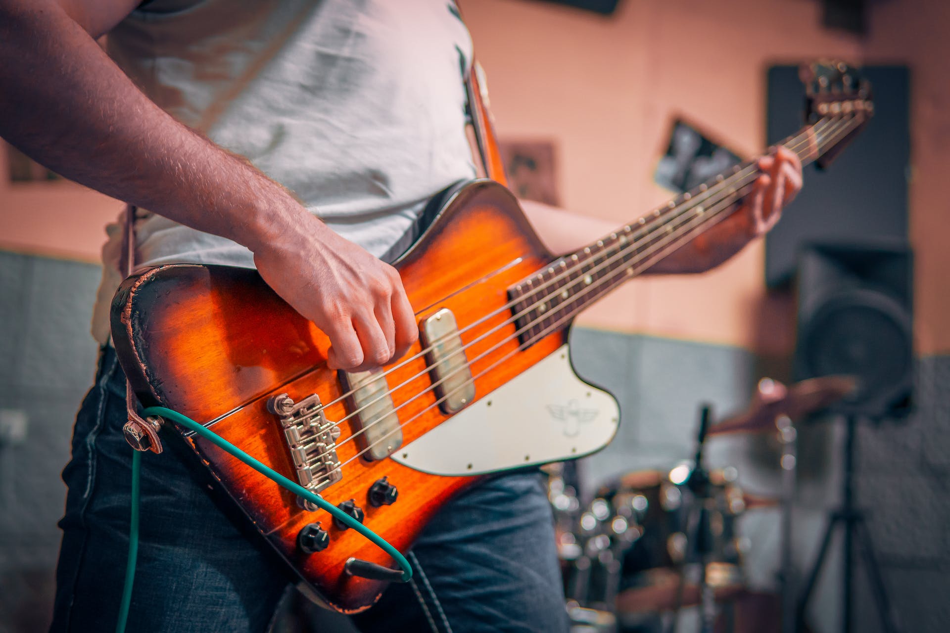 Ein Bassist mit hellem T-Shirt spielt auf einem e-Bass mit roetlichem Korpus