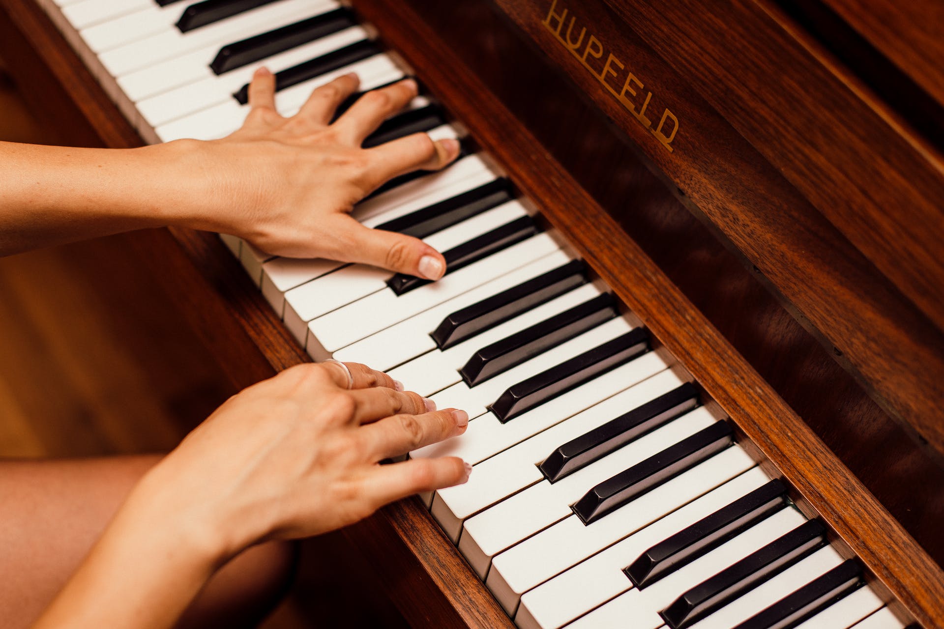 Zwei Haende spielen auf der weissen Tastatur eines braunen Hupfeld Pianos