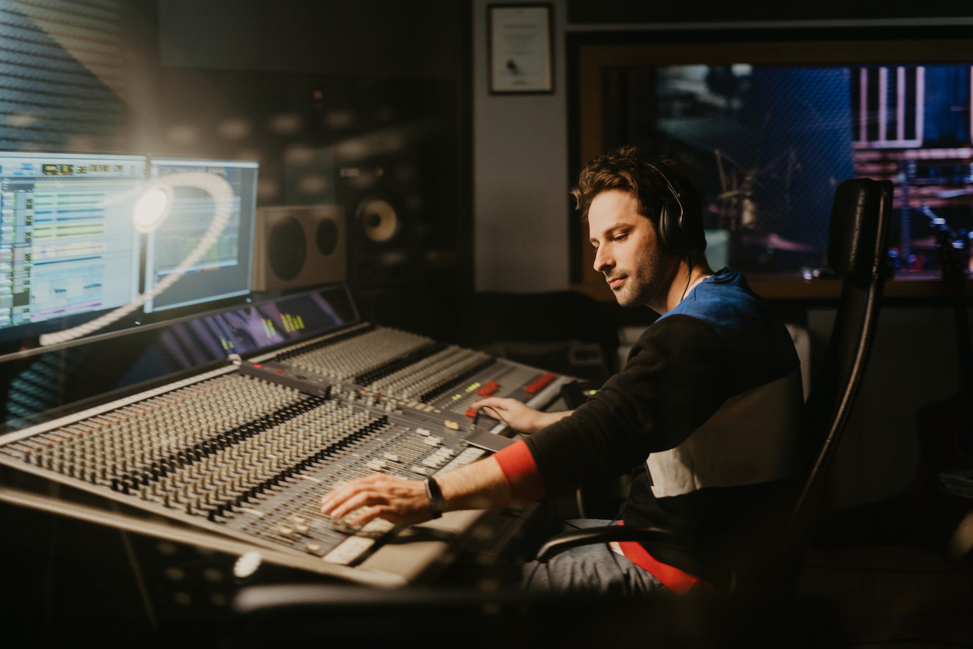 Mixing-Engineer sitzt vor einem grossen Mischpult und bedient die Drehregler und Fader