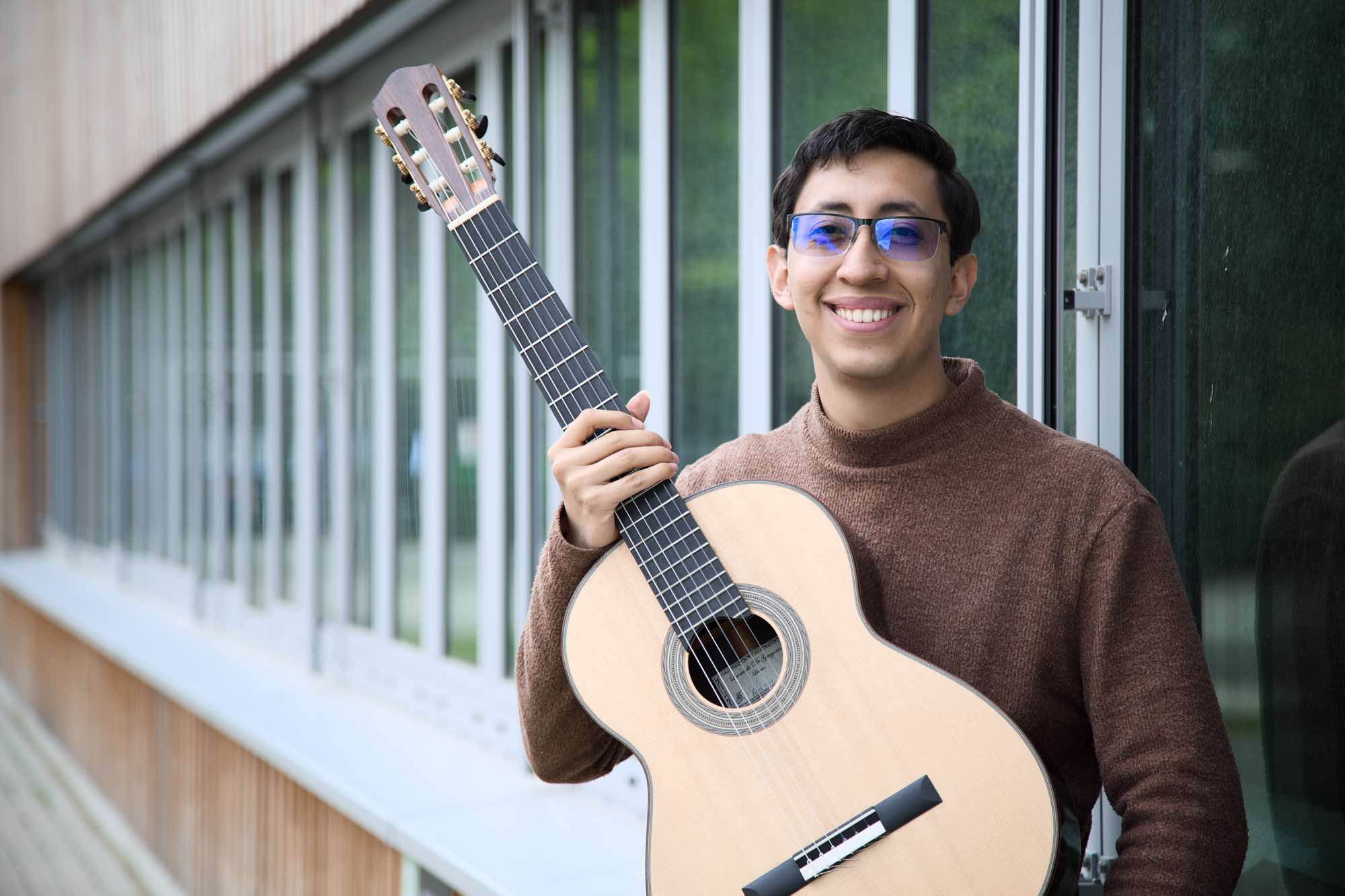 Jhostin Guzmán - Jhostin Guzman hält eine Akustikgitarre in den Händen auf dem Geländer der Rheinhöfe.