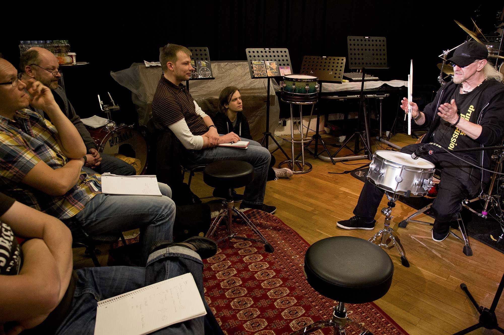 Manni von Bohr sitzt mit Stoecken in der Hand vor einer Snaredrum und erklaert den Workshop-Teilnehmern alles zum Thema Drumtuning.