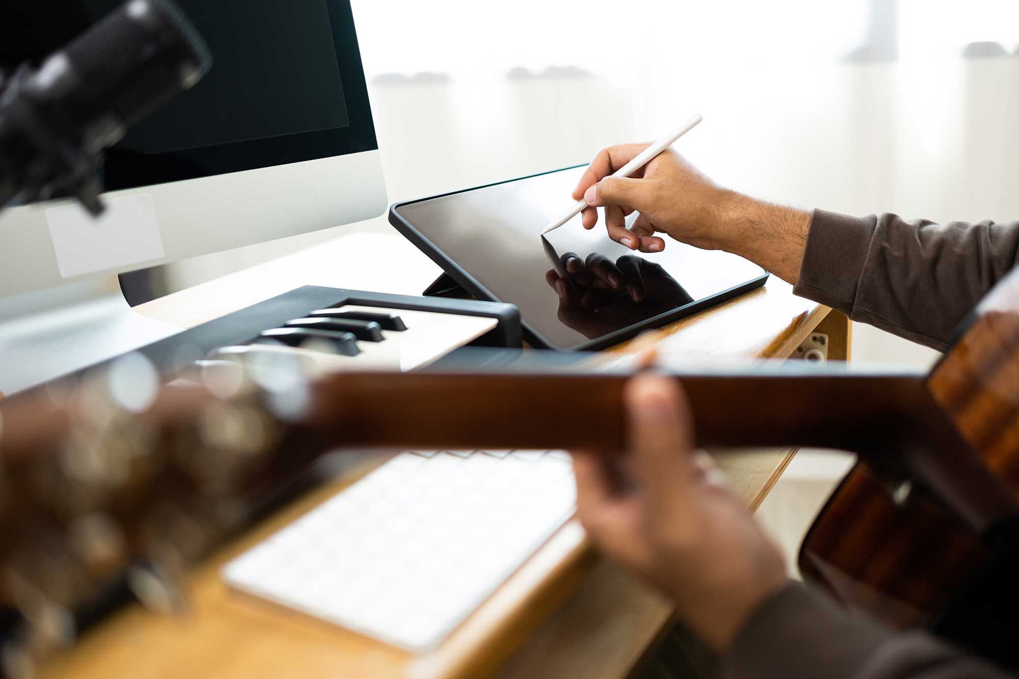 Ein Musiker sitzt mit seiner Gitarre vor einem Tisch mit iPad, Monitor und Keyboard-Tastatur.