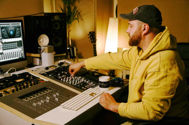 Workshops / Logic Po X - Online-Workshop - Tim Bremer sitzt vor einem Monitor und einem Mischpult und mischt einen Song mit Logic Pro X